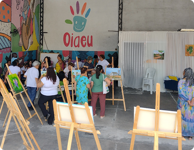 Oficina de artes da OIAEU com participantes ao redor de cavaletes